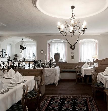 Gemütliches Restaurant im rustikalen Stil mit Holzvertäfelungen und eleganten Kronleuchtern. Weiße Tischdecken und gefaltete Servietten dekorieren die Tische.