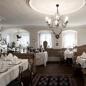 Ristorante elegante con tavoli apparecchiati con tovaglie bianche, sedie in legno, decorazioni a tema naturale e luci soffuse di un lampadario.