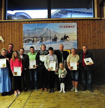 Un gruppo di persone posa con certificati in una sala rivestita in legno. Una bambina è al centro. Sullo sfondo, opere d'arte equestri.