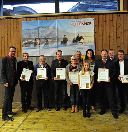 Un gruppo di persone in una sala di legno tiene dei certificati in mano. Sullo sfondo, un grande poster raffigura cavalli in un paesaggio innevato.