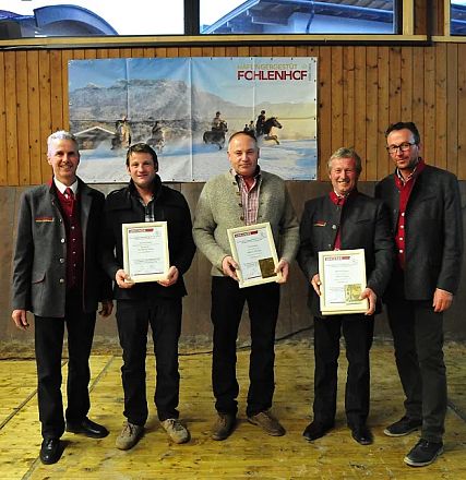 Cinque uomini in giacca e cravatta posano con certificati in una sala con pannelli di legno e poster di cavalli alle pareti.