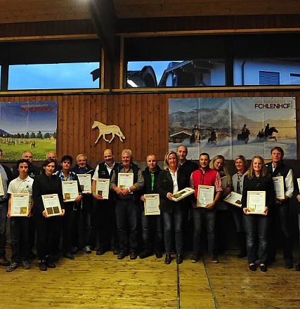 Un gruppo di persone in uno spazio chiuso tiene in mano certificati. Sullo sfondo ci sono poster di cavalli e un ambiente rurale.