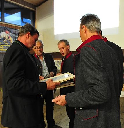 Quattro uomini in giacca parlano in una sala conferenze. Uno tiene in mano un documento. Sullo sfondo ci sono scatole e una grande finestra.