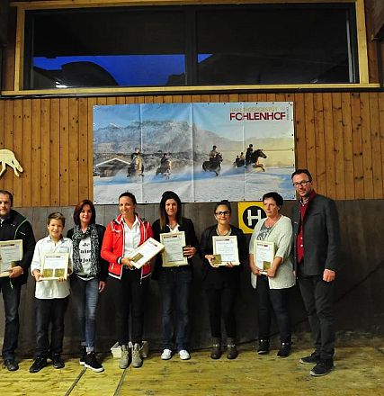 Gruppo di persone in piedi su un palcoscenico, ciascuno con un certificato in mano. Sorridono verso la telecamera. Alle spalle un grande poster di cavalli.