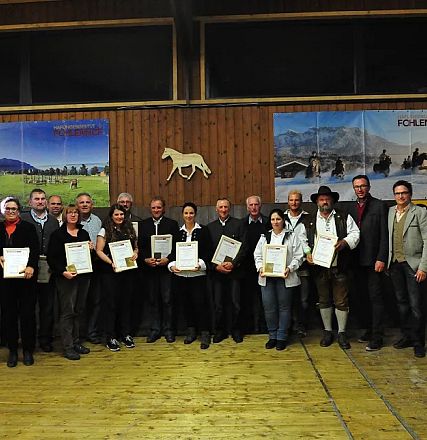 Un gruppo di persone in posa in una stanza rustica. Alcuni tengono dei certificati, sullo sfondo poster con immagini di cavalli e montagne.