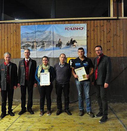 Sei persone in piedi in una sala ricreativa con pannelli in legno e un poster con cavalli sullo sfondo, alcune con certificati in mano.