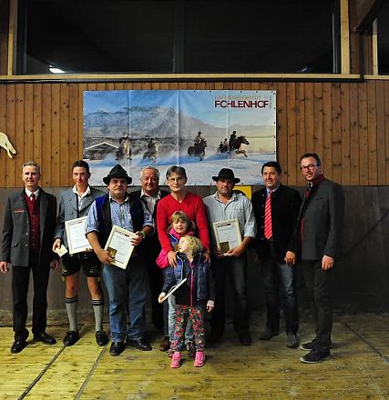 Gruppo di persone in posa in una struttura al coperto, alcuni tengono certificati. Sullo sfondo ci sono poster di cavalli su una parete di legno.