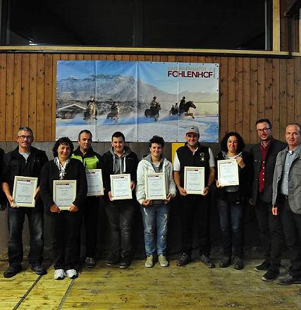 Un gruppo di persone posa con certificati in mano in una sala in legno. Sullo sfondo, un grande poster con paesaggi e un cavallo appeso alla parete.
