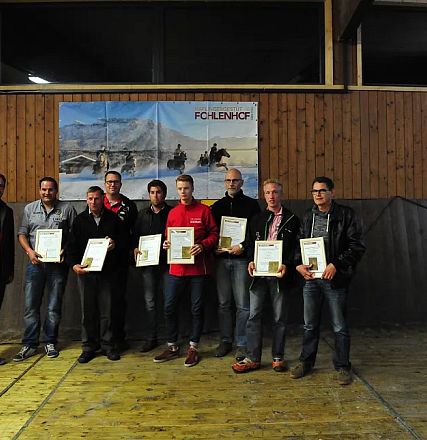 Un gruppo di uomini in piedi, ciascuno con un certificato in mano, in una sala di legno. Alle pareti, poster colorati e una figura di cavallo stilizzato.