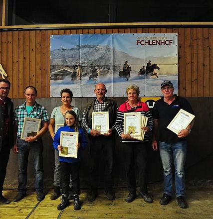 Un gruppo di persone posa con certificati in una sala di legno. Sullo sfondo, manifesti e un logo con un cavallo. Atmosfera di celebrazione.