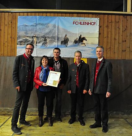 Cinque persone posano sorridenti in una sala con un poster di cavalli sullo sfondo. Una donna tiene un certificato in mano.