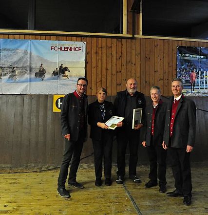 Un gruppo di cinque persone in posa davanti a un palco di legno, con quadri appesi sullo sfondo. Uno tiene in mano una targa o un riconoscimento.