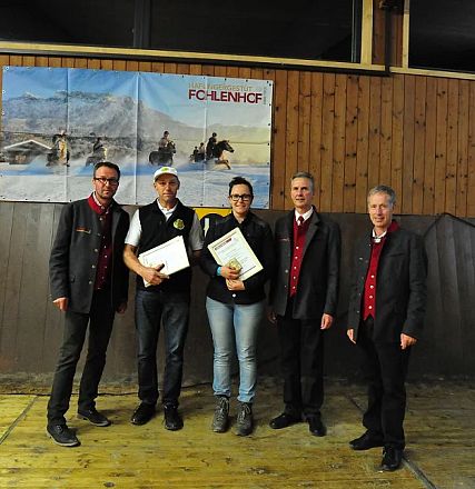 Cinque persone in posa in una sala con pareti di legno, tre uomini in abiti formali e due persone con premi o attestati. Foto di gruppo informale.