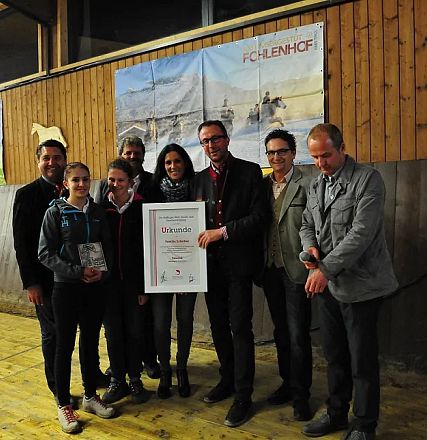 Un gruppo di persone posa sorridendo per una foto in un ambiente rustico. Uno di loro tiene un diploma, dietro si vedono poster di cavalli su legno.