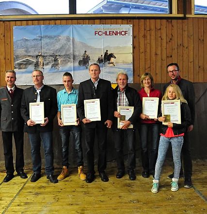 Un gruppo di persone in posa con certificati in mano, all'interno di un edificio con pannelli di legno e poster sullo sfondo. Atmosfera formale.