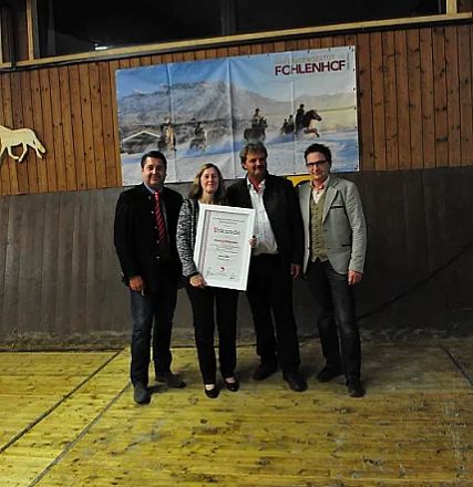 Quattro persone posano felicemente all'interno di una sala con una targa. Sullo sfondo un pannello dipinto raffigura scene equestri.