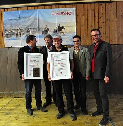Cinque uomini in giacca posano sorridenti con due certificati incorniciati. Sullo sfondo, una parete di legno e un poster con cavalli.