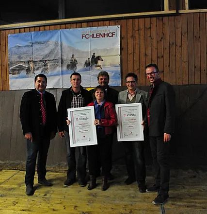 Un gruppo di persone sorride per una foto di gruppo al chiuso. Due persone tengono in mano dei certificati incorniciati. Sullo sfondo un quadro di cavalli.