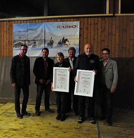 Sei persone posano con certificati davanti a un grande poster di cavalli su un muro di legno. Sono vestite in modo formale e sorridono alla fotocamera.