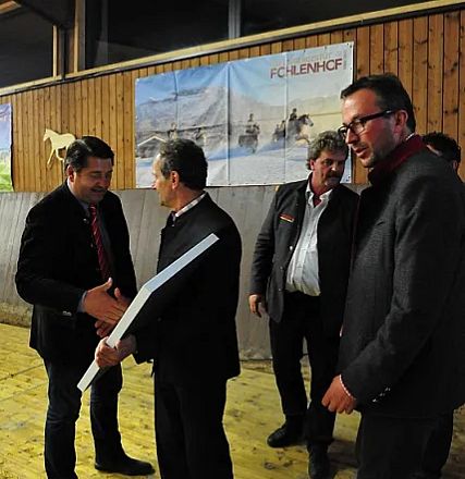 Uomini in abiti eleganti si stringono la mano in una sala con pareti di legno, dove sono appesi dei quadri. Sembra un incontro formale o una riunione.