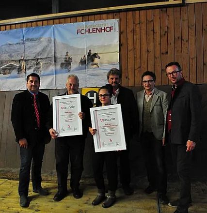 Gruppo di sei persone in piedi, due tengono cornici con certificati, sullo sfondo un'immagine di montagna e cavalli, atmosfera informale.