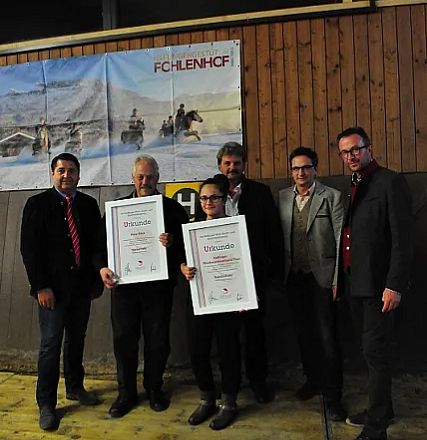 Sei persone in piedi sorridono, tenendo cornici con certificati. Sono in un interno con un poster di cavalli invernali sulla parete.