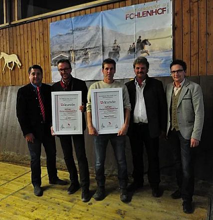 Gruppo di cinque persone in piedi, due al centro tengono dei certificati incorniciati. Sfondo di legno con foto di cavalli sopra di loro.