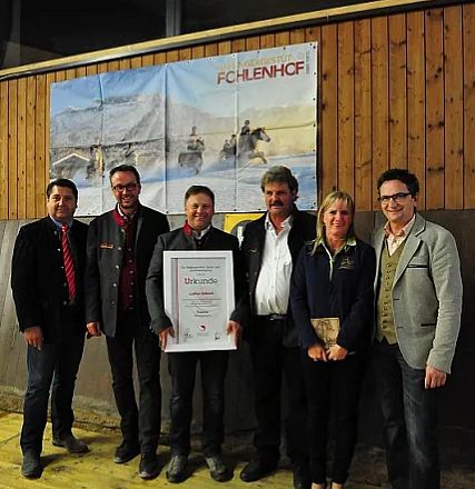 Gruppo di persone in posa, alcune con una cornice di certificato in mano. Sono in piedi davanti a un pannello di legno e un grande poster sullo sfondo.