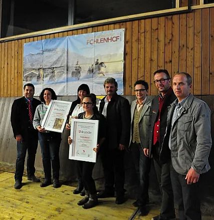Gruppo di persone in posa con certificati in mano, davanti a un poster di cavalli in un ambiente con pannelli di legno.