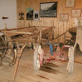 Ein rustikales Museum mit traditionellen landwirtschaftlichen Geräten wie Pflügen und Wagen aus Holz. Die Wände sind mit alten Fotos und Schildern dekoriert.