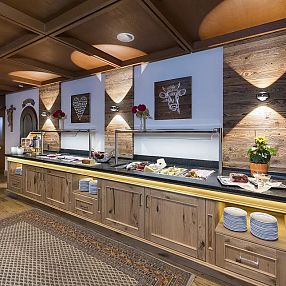 Rustikales Buffet mit Holzmöbeln, dekorativen Holzwänden und abgedeckten Speisen. Ein Blumenarrangement und ein Holzfass sind ebenfalls zu sehen.