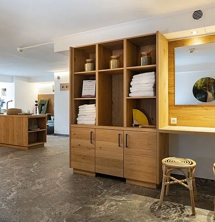 Modernes Interieur einer Wellness-Oase mit Holzmöbeln, Handtüchern und Pflanzen. Die schlichte Einrichtung schafft eine ruhige, entspannende Atmosphäre.