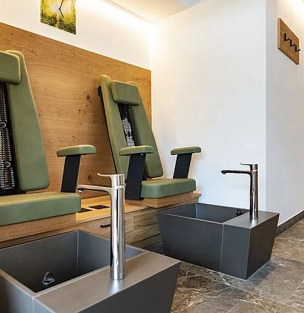 Ein moderner Wellnessbereich mit ergonomischen Stühlen und Fußbecken mit Wasserhähnen. Die Einrichtung ist in warmen Naturtönen gehalten.