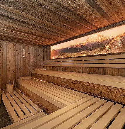 Holzverkleidete Sauna mit mehreren Sitzbänken. Ein beleuchtetes Bild von Bergen schmückt die Wand, sorgt für eine entspannende Atmosphäre.