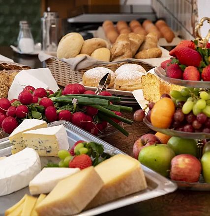 Ein reichhaltiges Frühstücksbuffet mit verschiedenen Brotsorten, Käse, frischem Obst, Radieschen und Gebäck auf einem Tisch arrangiert.