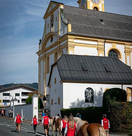 Historische Kirche mit gelben Verzierungen, davor ein kleineres Gebäude mit einem Fenster. Der Himmel ist blau und die Sonne scheint hell.