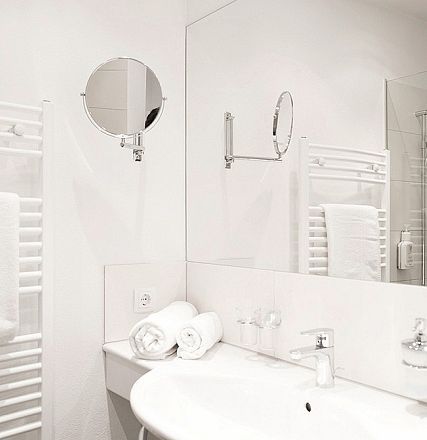 Modernes Badezimmer mit weißem Design. Ein Waschbecken mit Handtuch und Seifenspender sind zu sehen. Ein großer Spiegel reflektiert die Wandfliesen.