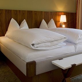 Camera d'albergo accogliente con letto matrimoniale, cuscini soffici, illuminazione calda e arredi moderni in legno.