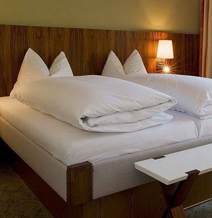 Gemütliches Hotelzimmer mit einem King-Size-Bett, zwei Nachttischen mit Lampen, Holzwandvertäfelung und Vorhängen. Warme, einladende Atmosphäre.