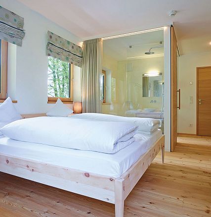 Helles, modernes Schlafzimmer mit Holzmöbeln, Doppelbett und großen Fenstern. Das Interieur strahlt eine gemütliche und natürliche Atmosphäre aus.