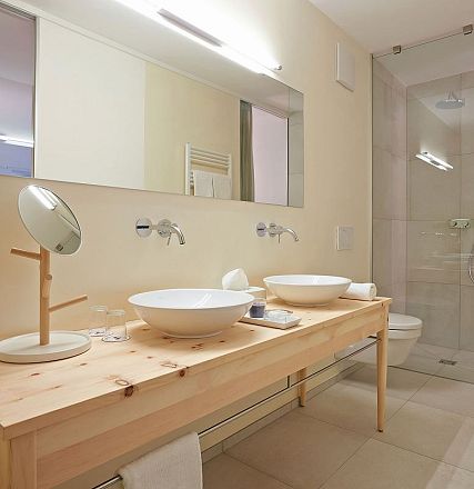 Modernes Badezimmer mit zwei Waschbecken auf einem Holztisch, großen Spiegeln und einer ebenerdigen Dusche in neutralen Farben gestaltet.