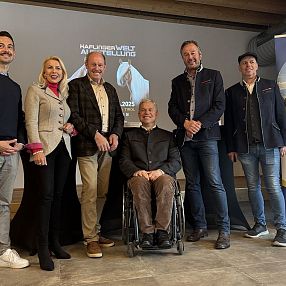 Gruppo di persone in posa davanti a poster e striscione nella sala conferenze. Vari stili di abbigliamento formale e casual, ambiente accogliente.
