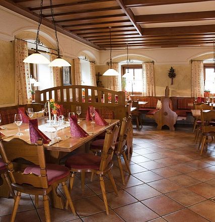 Gemütliches Restaurant im traditionellen Stil, Holzmöbel, gedeckte Tische mit roten Servietten, warme Beleuchtung, rustikale Dekoration an den Wänden.