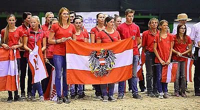 Gruppe von Menschen in roten T-Shirts hält die rot-weiß-rote Flagge von Österreich in einer Halle. Sie stehen dicht beieinander und schauen in die Kamera.