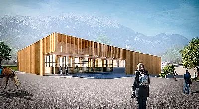 Modernes Gebäude aus Holz mit großen Glasflächen und Bergen im Hintergrund. Menschen stehen oder gehen in der Nähe des Eingangs. Blauer Himmel.